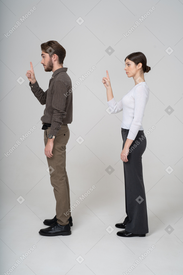 Side view of a young couple in office clothing raising finger