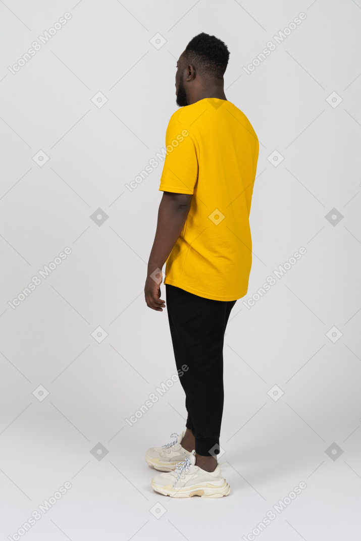 Vista posterior de tres cuartos de un joven de piel oscura con camiseta amarilla parado