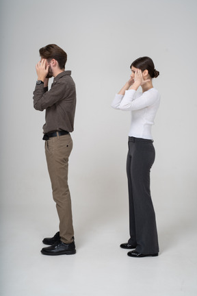 Side view of a shocked young couple in office clothing touching head