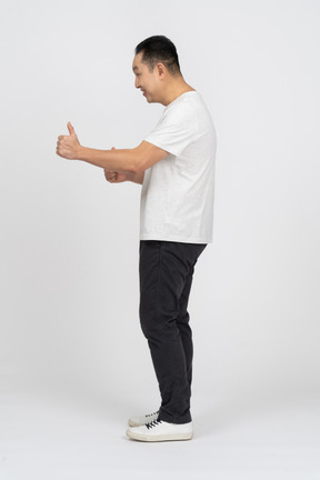 Vista lateral de un hombre feliz con ropa informal que muestra el pulgar hacia arriba