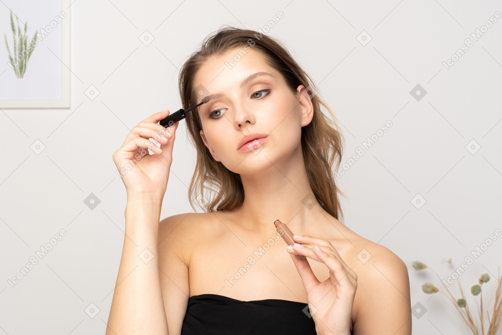 Front view of a young woman wearing black top holding brushing her eyebrows