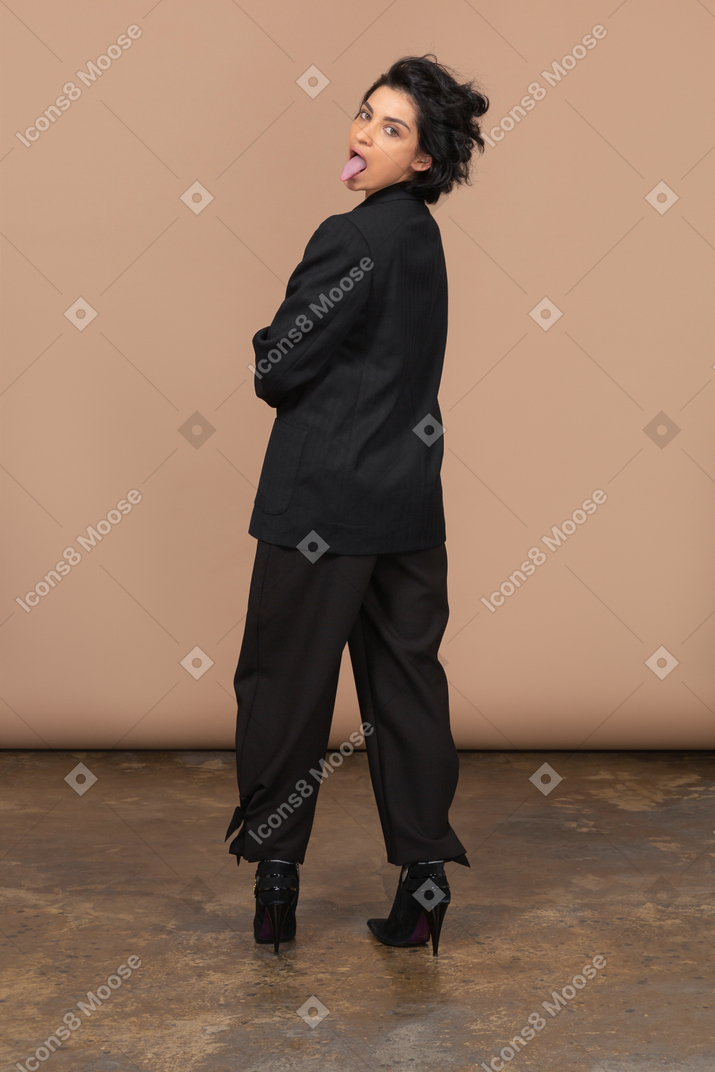Vista traseira de uma empresária usando terno preto e mostrando a língua enquanto olha para a câmera