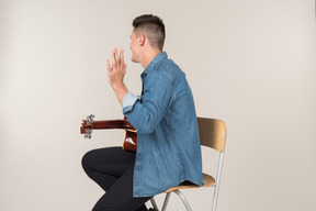 Young guy sitting on the table in profile and playing on guitar