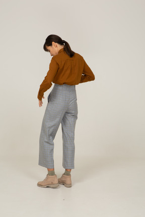 Three-quarter back view of a young asian female in breeches and blouse looking down