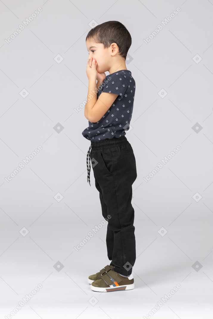 Side view of a cute boy covering mouth with hands