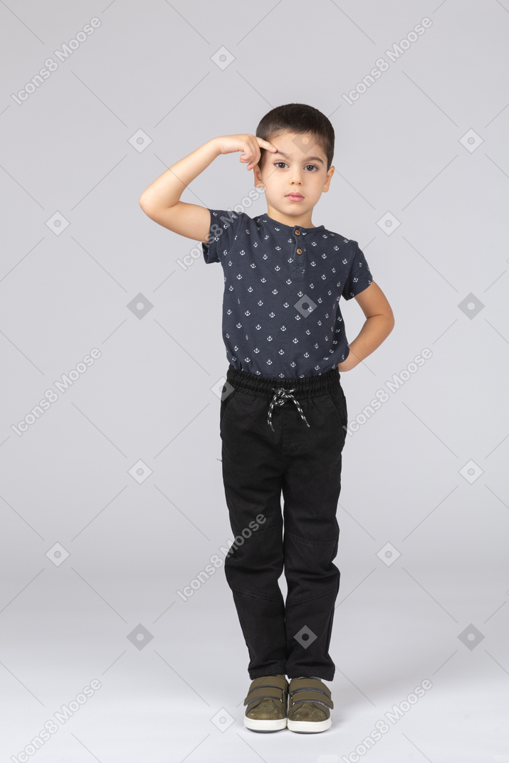 Front view of a cute boy in casual clothes pointing to forehead