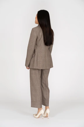 Three-quarter back view of a displeased young lady in brown business suit pressing lips