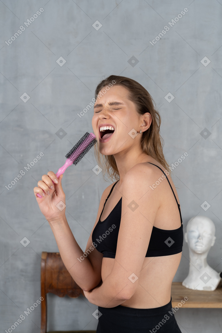 Portrait of an attractive young woman singing karaoke with hairbrush as mic