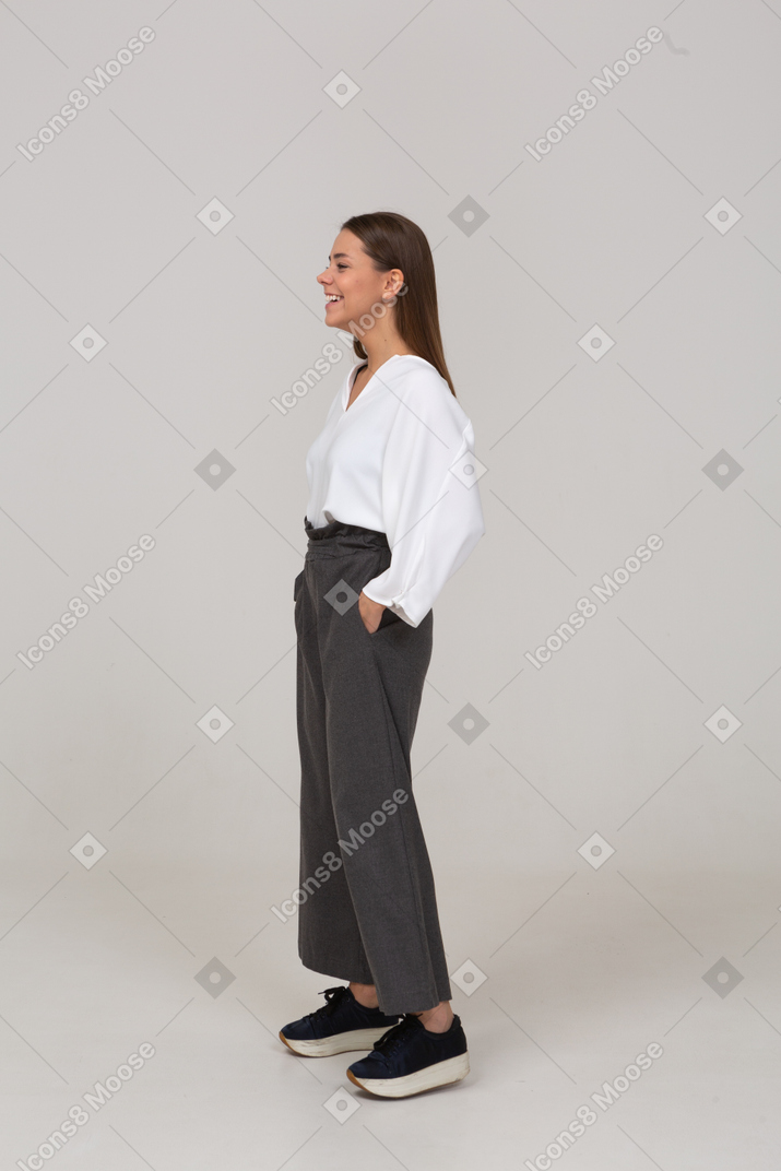 Three-quarter view of a smiling young lady in office clothing putting hands in pockets