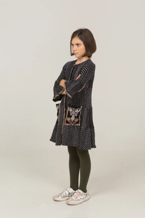 Three-quarter view of an offended little girl in dress crossing arms