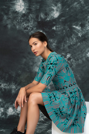 Tired woman in turquoise dress sitting on a cube