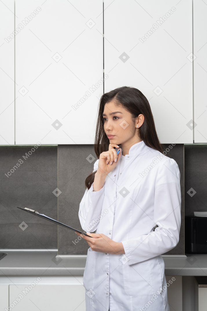 一位年轻的女医生，抚摸下巴，一边看一边拿着平板电脑的四分之三视图