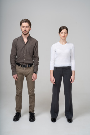 Front view of a young couple in office clothing standing still with her eyes closed