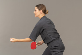 Вид сбоку молодой женщины в комбинезоне, обслуживающей теннисный мяч