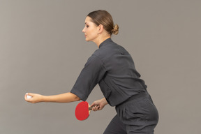 Side view of young woman in a jumpsuit serving tennis ball