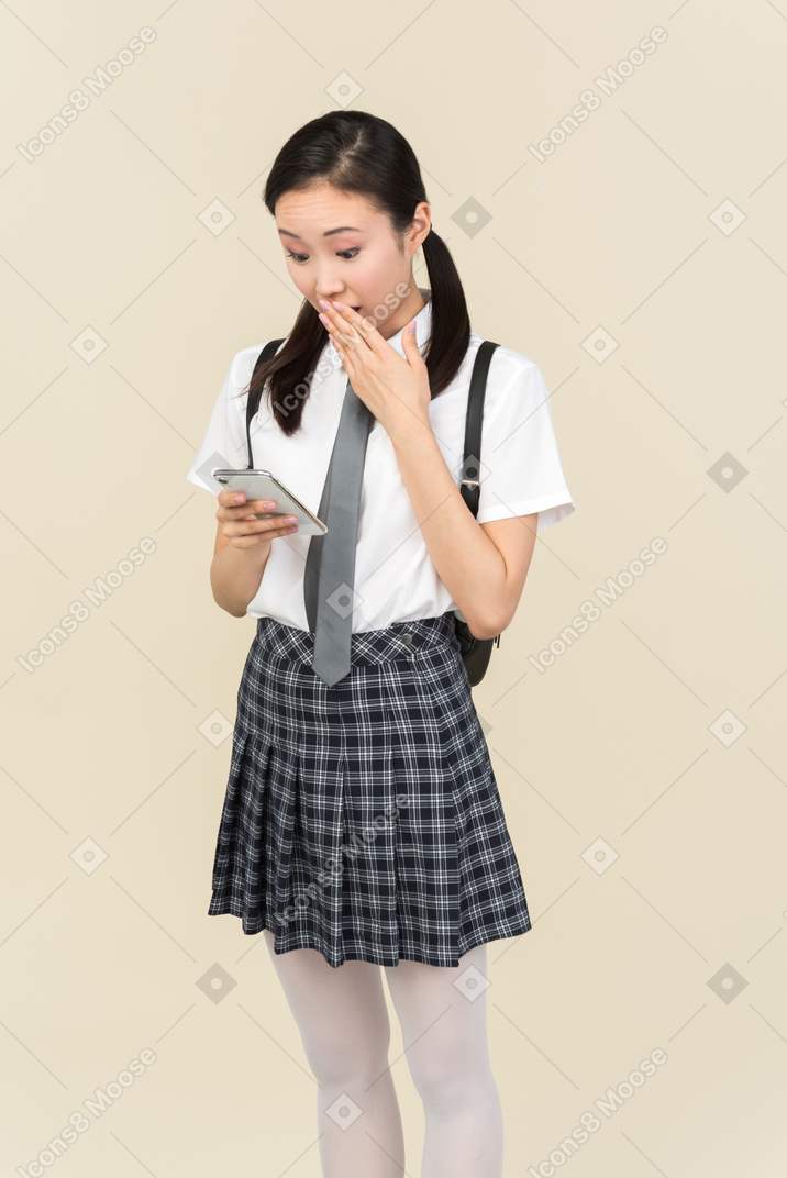 Menina da escola asiática ofegante enquanto estiver usando smartphone