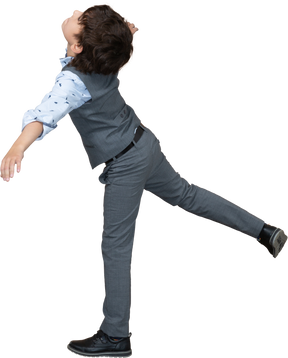 Vista lateral de um menino de terno equilibrando em uma perna com os braços estendidos