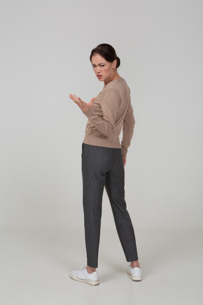 Three-quarter back view of a gesticulating questioning young lady in beige pullover