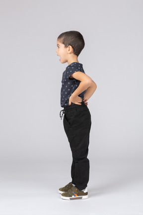 Vista lateral de um menino lindo de criança em pé com as mãos nos quadris