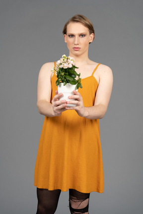 Portrait of a young genderfluid person in dress giving away pot of flowers