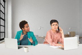 Two women sitting at a table with laptops