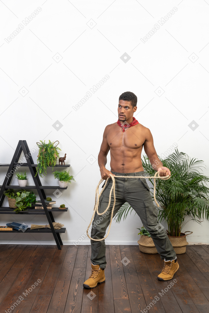 Athletic young man standing with feet wide apart and holding a rope