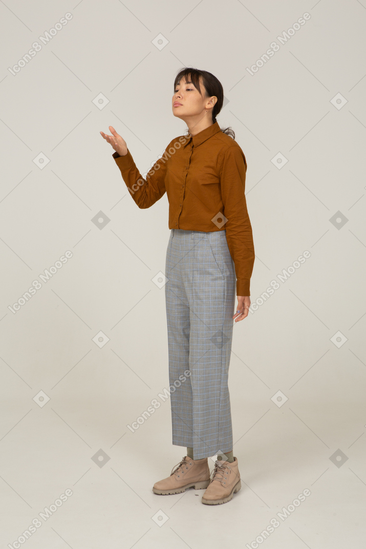 Vista di tre quarti di una giovane donna asiatica in calzoni e camicetta che alza la mano