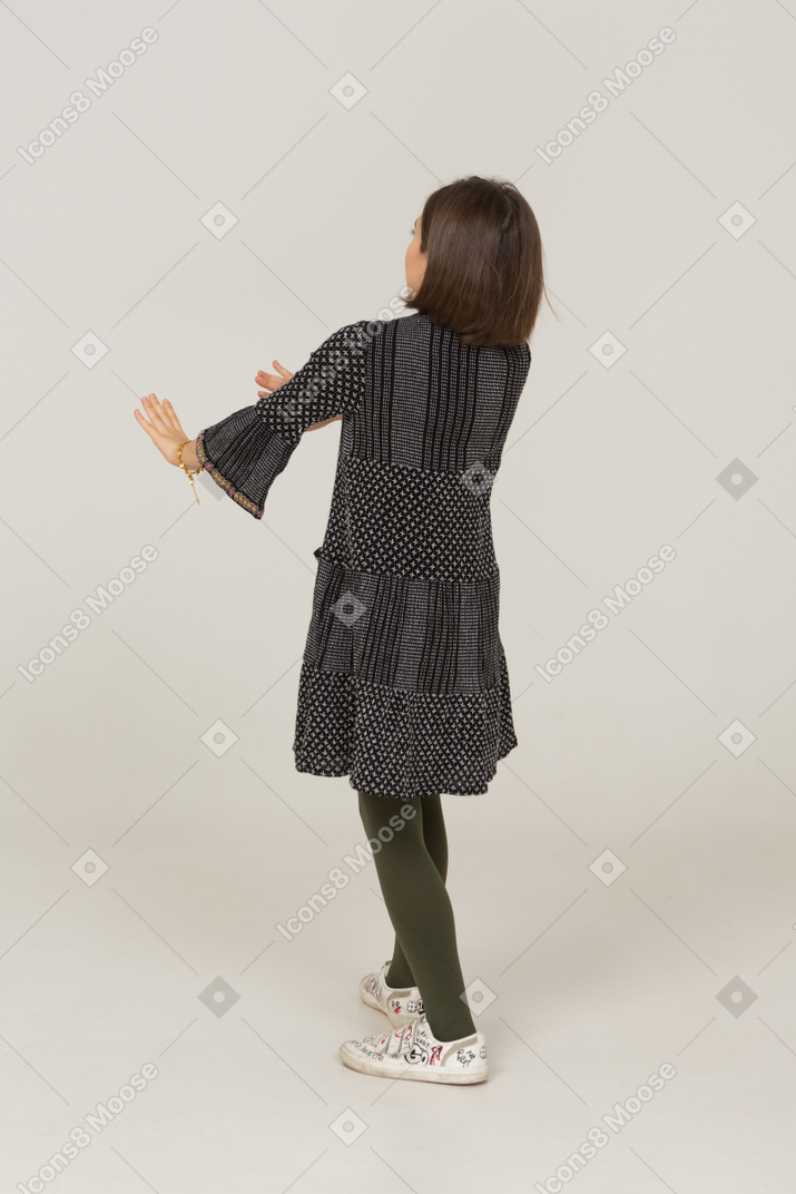 一个穿着裙子的小女孩伸出双臂的四分之三后视图