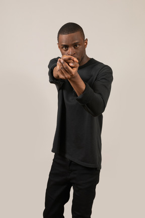 Front view of young man pretending to hold a gun and aiming