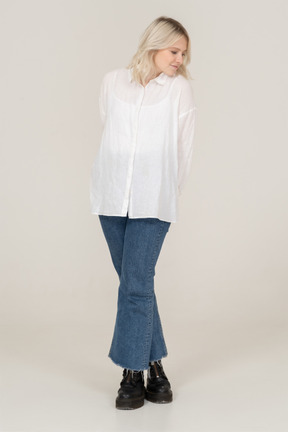 Front view of a shy blonde female in casual clothes crossing legs and looking down