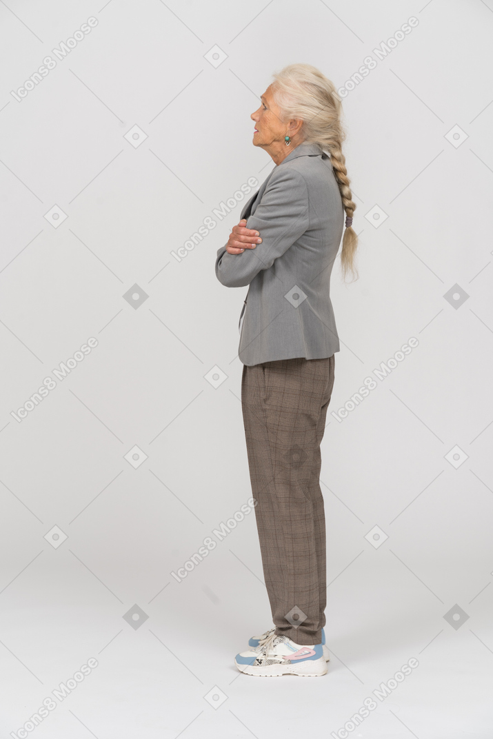 Vista laterale di una vecchia signora in abito in posa con le braccia incrociate