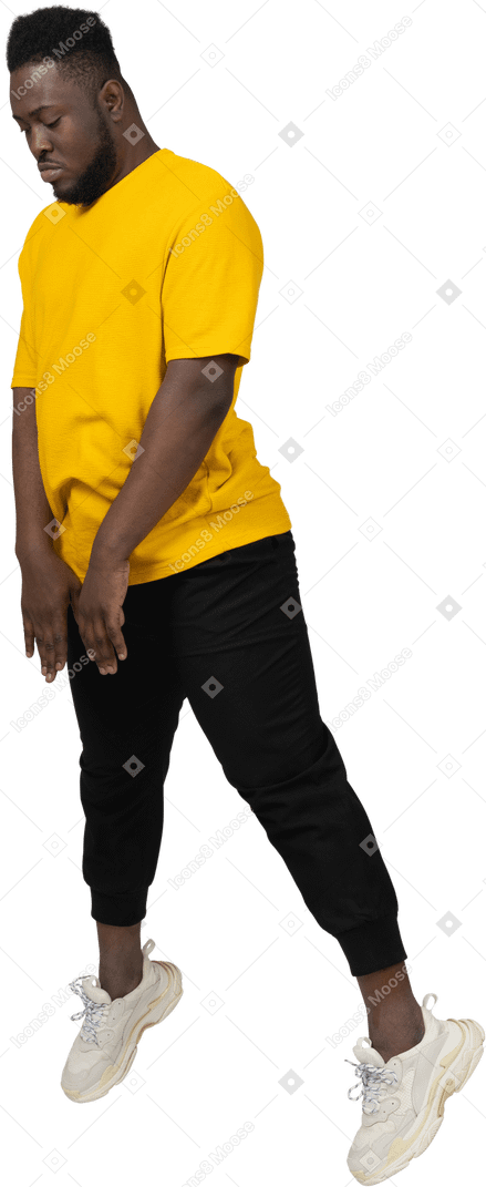 Three-quarter view of a jumping young dark-skinned man in yellow t-shirt looking down