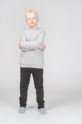 Front view of a thoughtful kid boy raising head and crossing hands