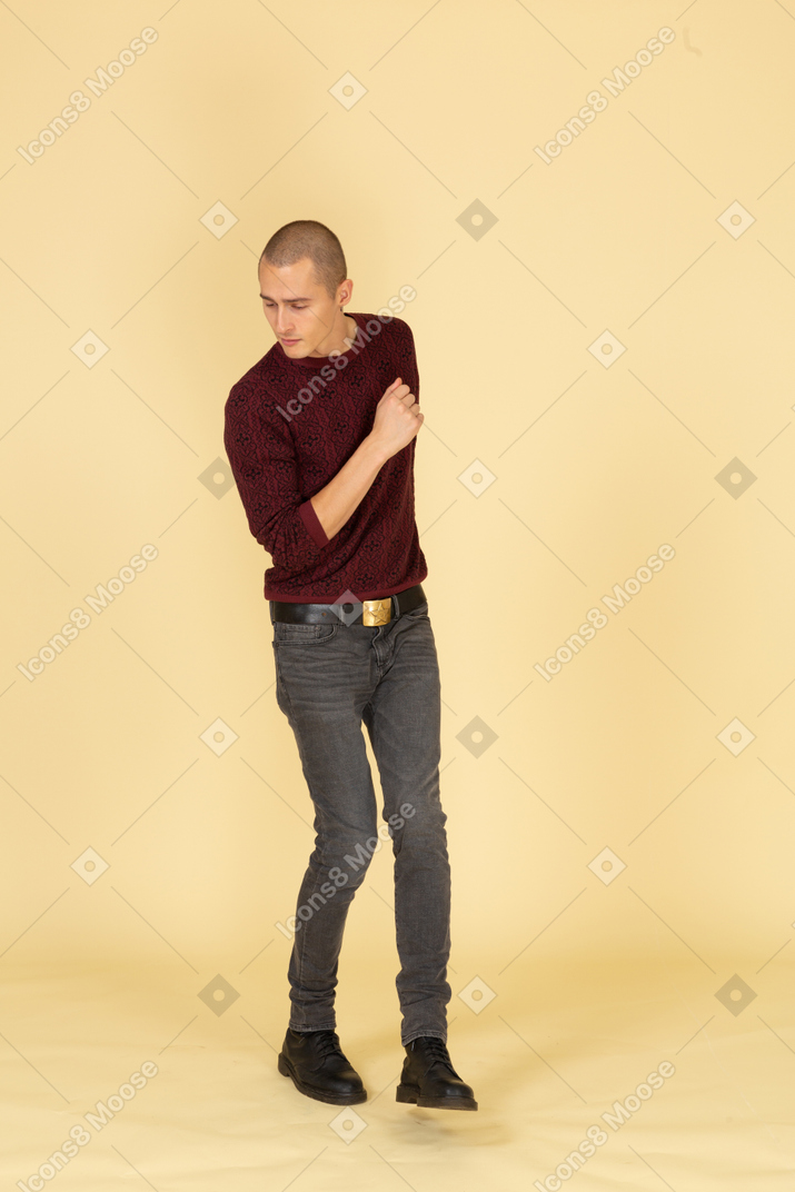 Front view of a dancing young man in red pullover raising leg