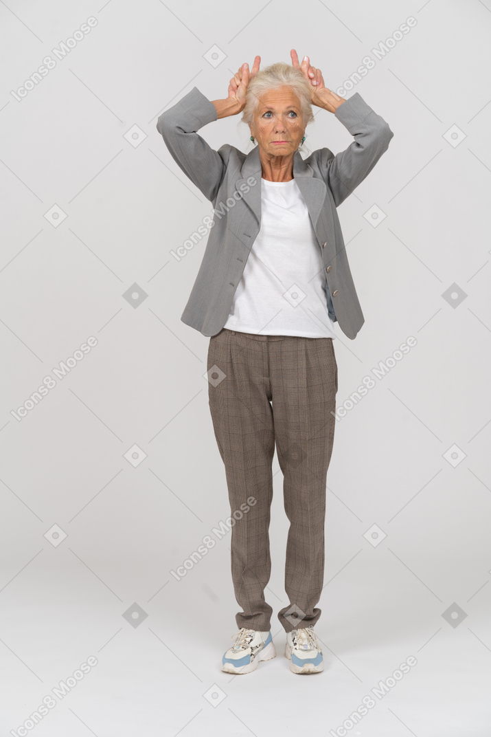 Vista frontal de una anciana en traje haciendo cuernos