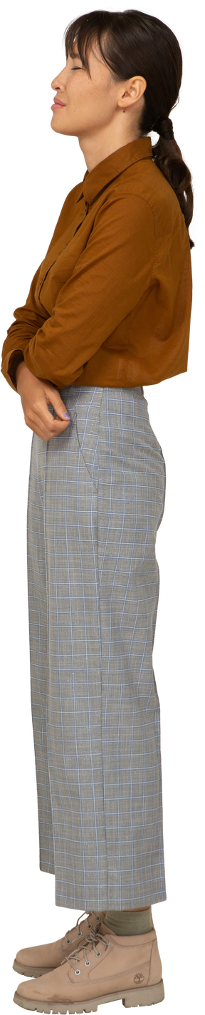 Vista laterale di una giovane donna asiatica stanca in calzoni e camicetta che incrociano le braccia