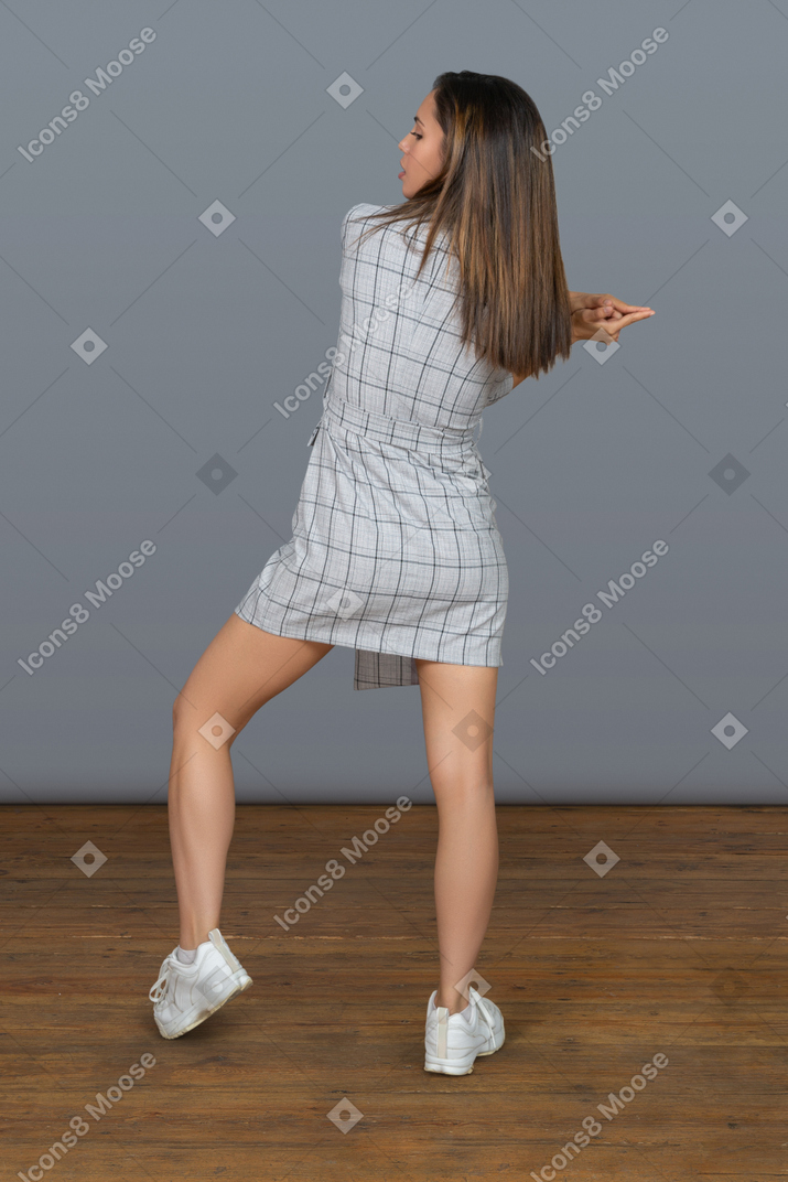 Sensual young woman making a handgun gesture while standing back to camera with feet shoulder width apart