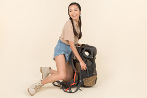 Junger asiatischer weiblicher reisender, der nahe sehr großem touristischem rucksack sitzt