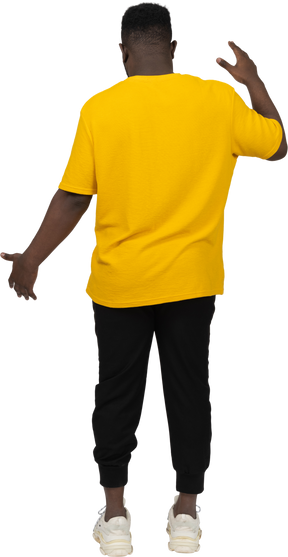 Vista posteriore di un giovane uomo dalla pelle scura in maglietta gialla che mostra le dimensioni di qualcosa