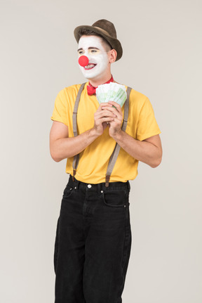 Cunning male clown holding money bills