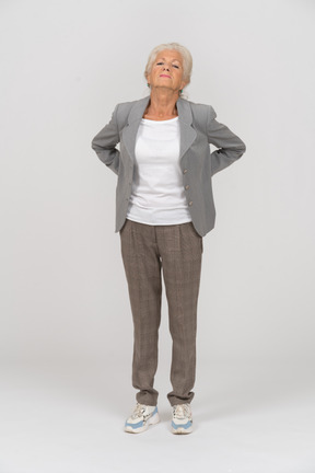Front view of an old lady in suit suffering from back ache