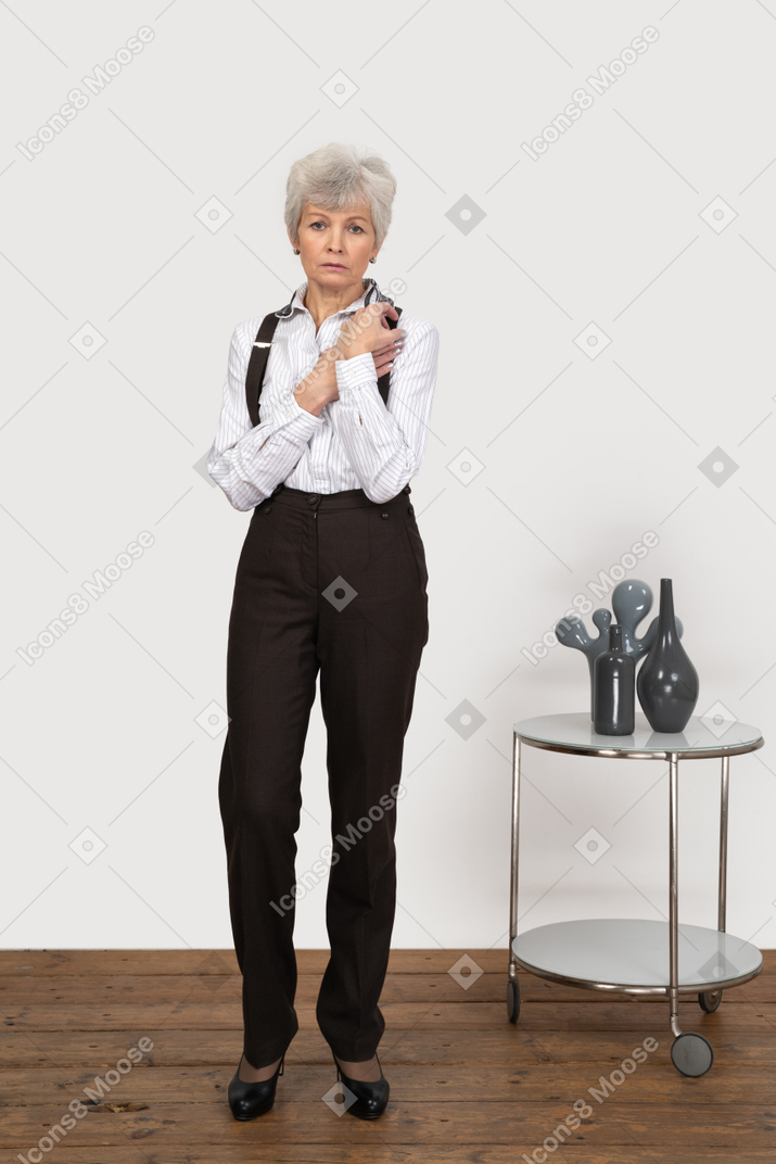 Front view of a worried old lady in office clothing holding hands together