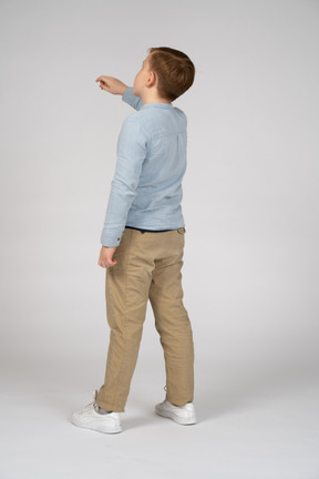Back view of young boy in shirt and pants raising his hand