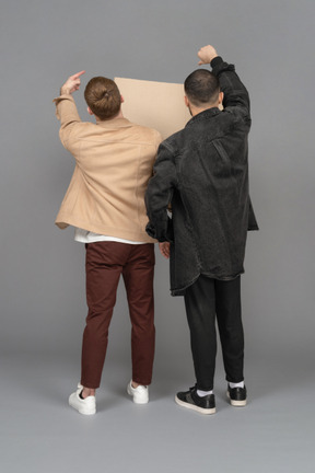 Vue arrière de deux jeunes hommes avec un panneau d'affichage agitant les mains avec passion