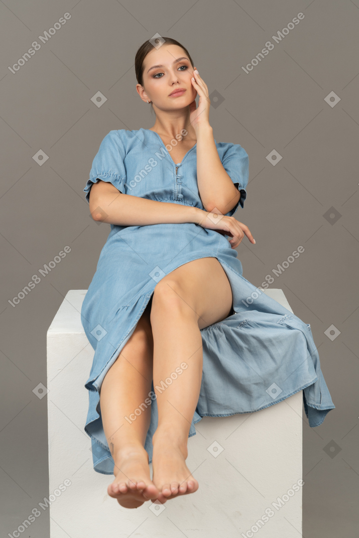 Vista frontale della giovane donna seduta sul cubo e guardando da parte