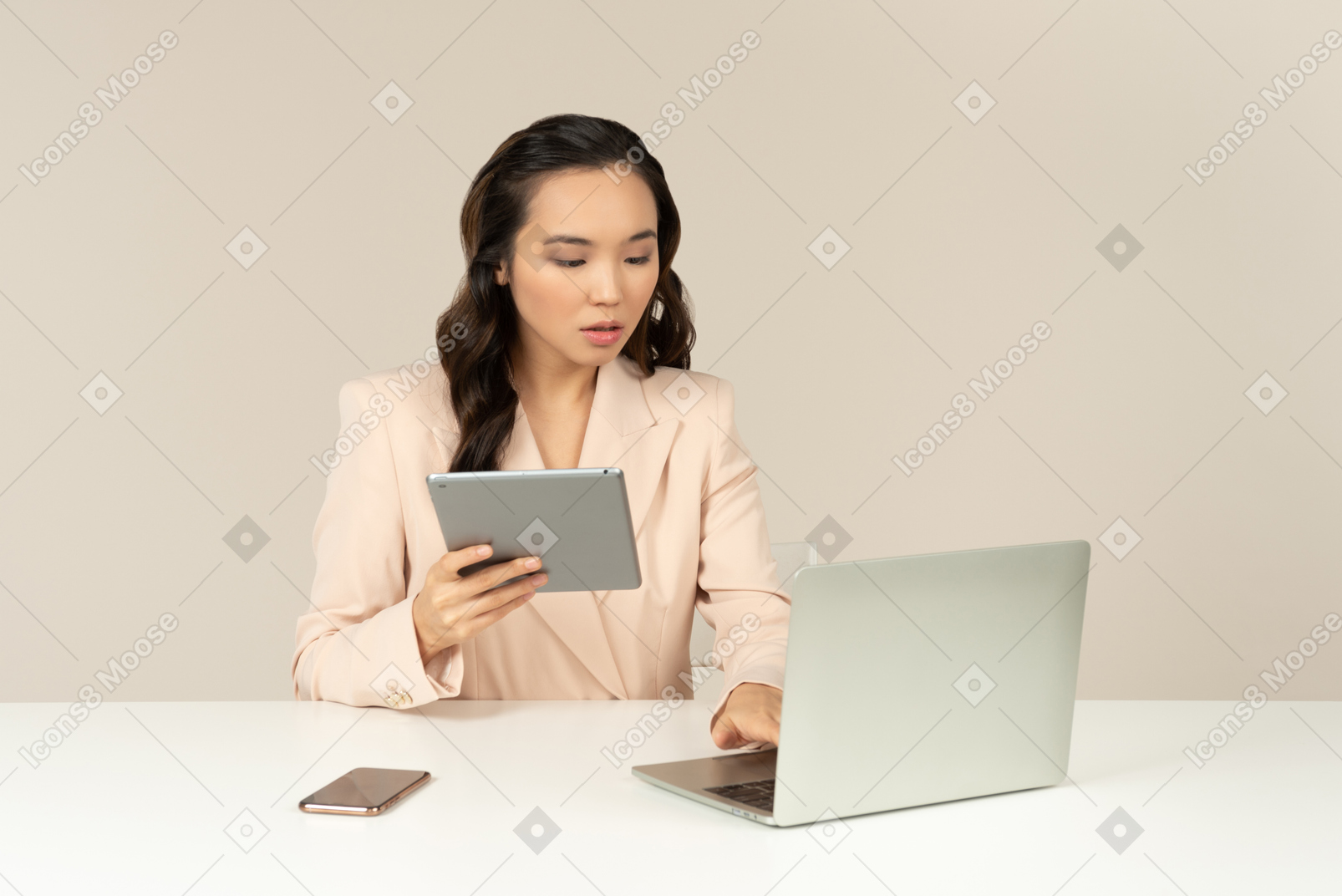 Asian female office employee working on laptop and holding tablet