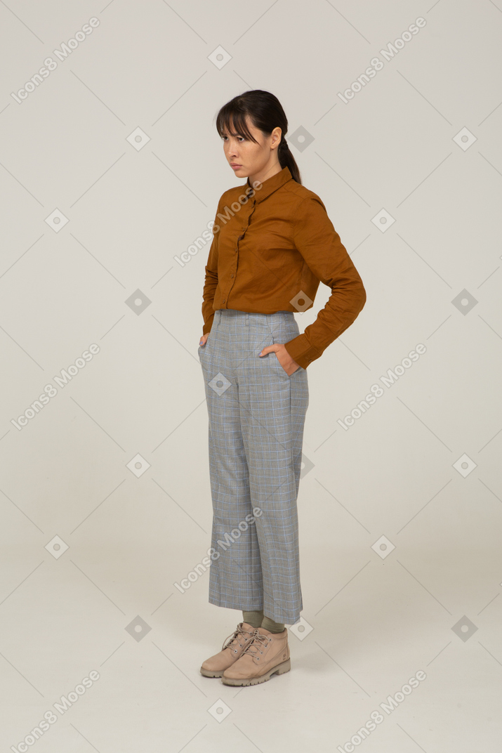 Vista de tres cuartos de una joven mujer asiática en calzones y blusa poniendo las manos en los bolsillos