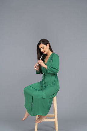 클라리넷을 연주하는 동안 의자에 앉아 녹색 드레스를 입은 젊은 아가씨의 전체 길이