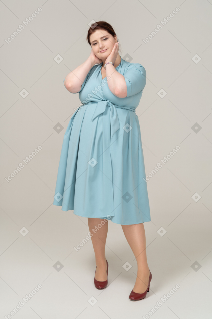 Front view of a woman in blue dress posing with hands on neck