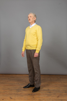 Vista de tres cuartos de un anciano vestido con jersey amarillo y parado